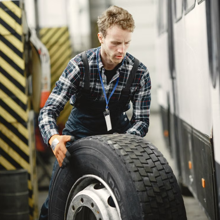 Mechanic lifts tire beside bus in garage.