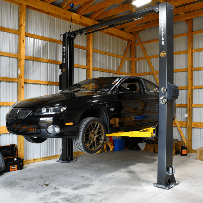 Black sports car lifted on garage hydraulic hoist.