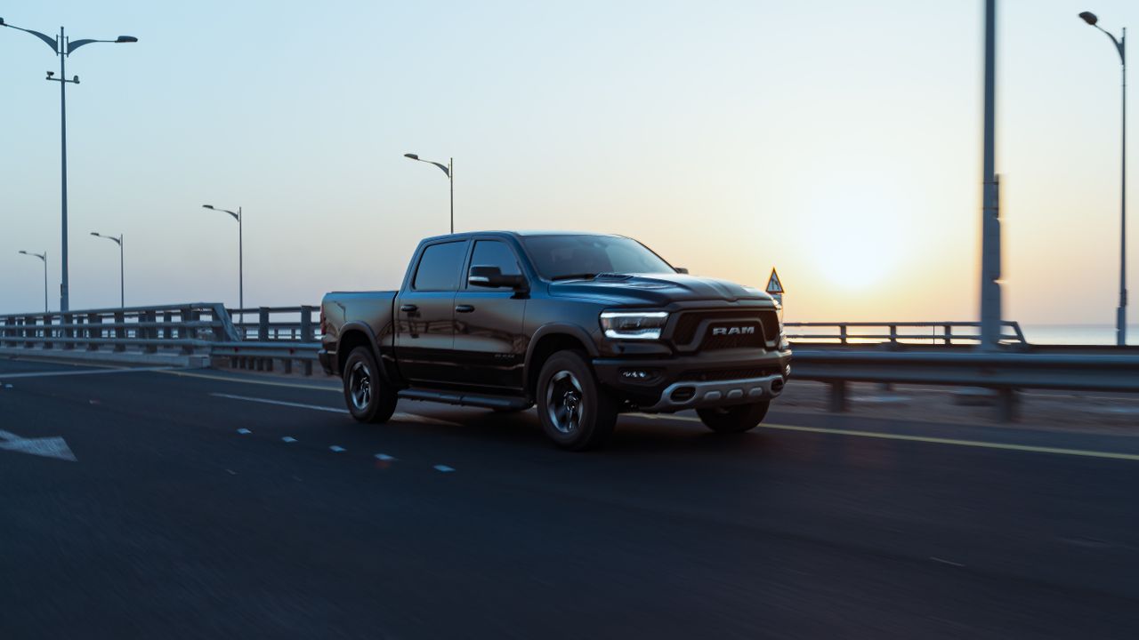 Black RAM pickup drives across bridge at sunset.
