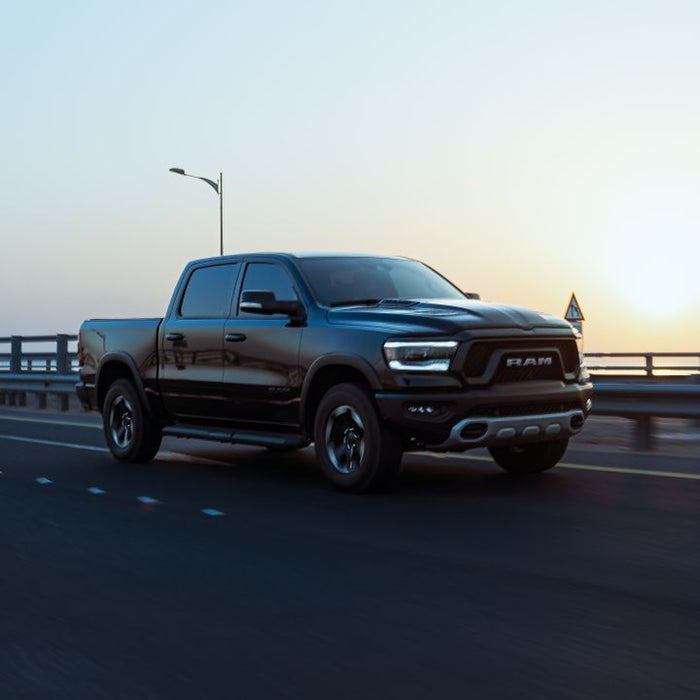 Black RAM pickup drives across bridge at sunset.