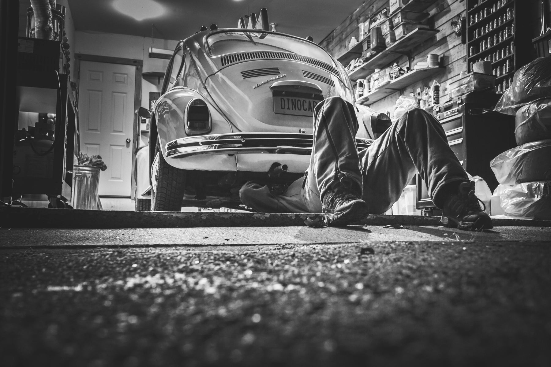 Mechanic working under vintage Beetle car in garage. 