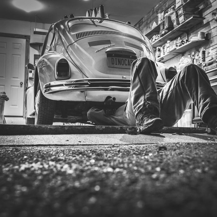 Mechanic working under vintage Beetle car in garage. 