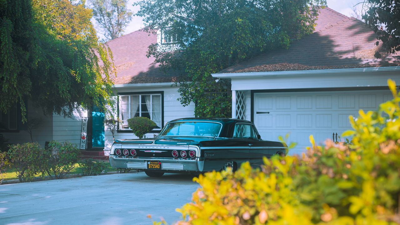 Classic car parked in suburban driveway beside garage.