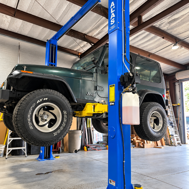 Atlas 9,000lb 2 psot lift with The Jeep is raised high, showing its tires and undercarriage. Customer install with HeavyLift Direct
